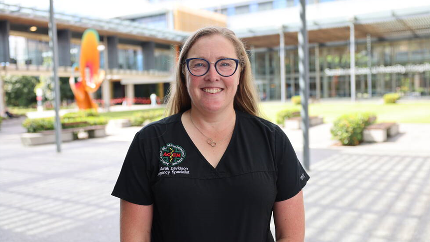 Headshot of a smiling woman in a black top wearing glasses in the courtyard outside Sunshine Coast University Hospital