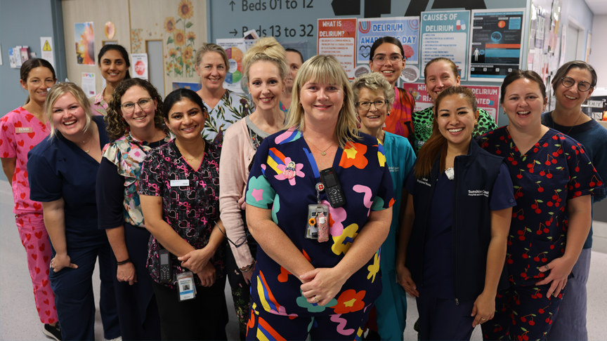 A group of nurses wearing different coloured scrubs, standing in front of a wall with Ward 4A written on it.