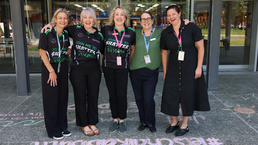 Five women stand with arms around each other outside Sunshine Coast University Hospital with chalk writing on the ground