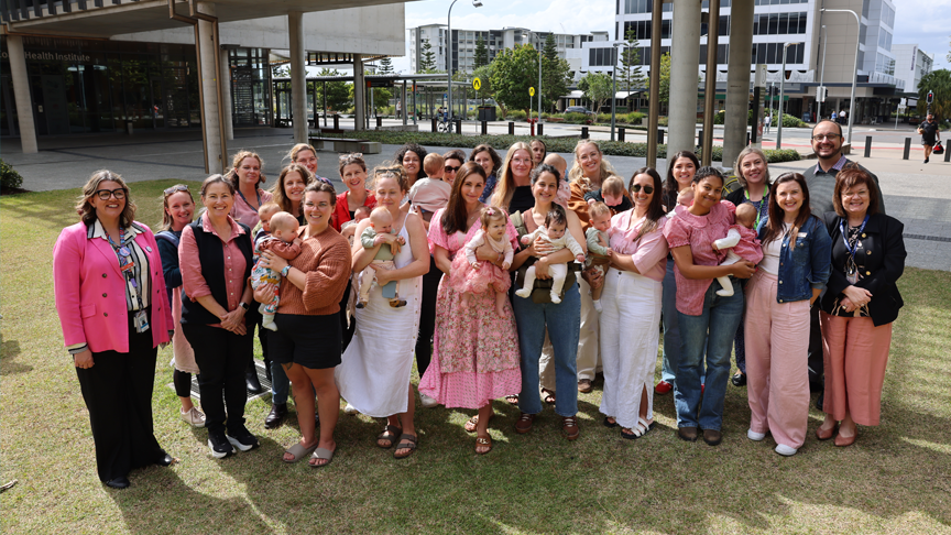 A large group of people, some holding babies, standing on the grass outside Sunshine Coast University Hospital