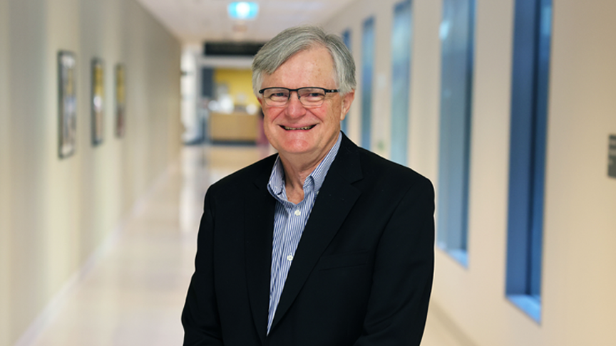 Headshot of Dr David Rowlands OAM smiling, standing in a hospital hallway.